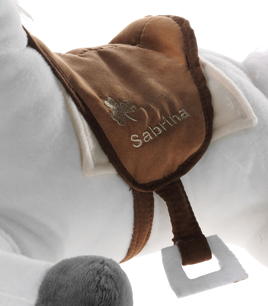 Plüschpferd mit personalisiertem Sattel Nahaufnahme eines Plüschpferdes mit einem braunen personalisierten Sattel, bestickt mit einem Kleeblatt und dem Namen Sabrina.